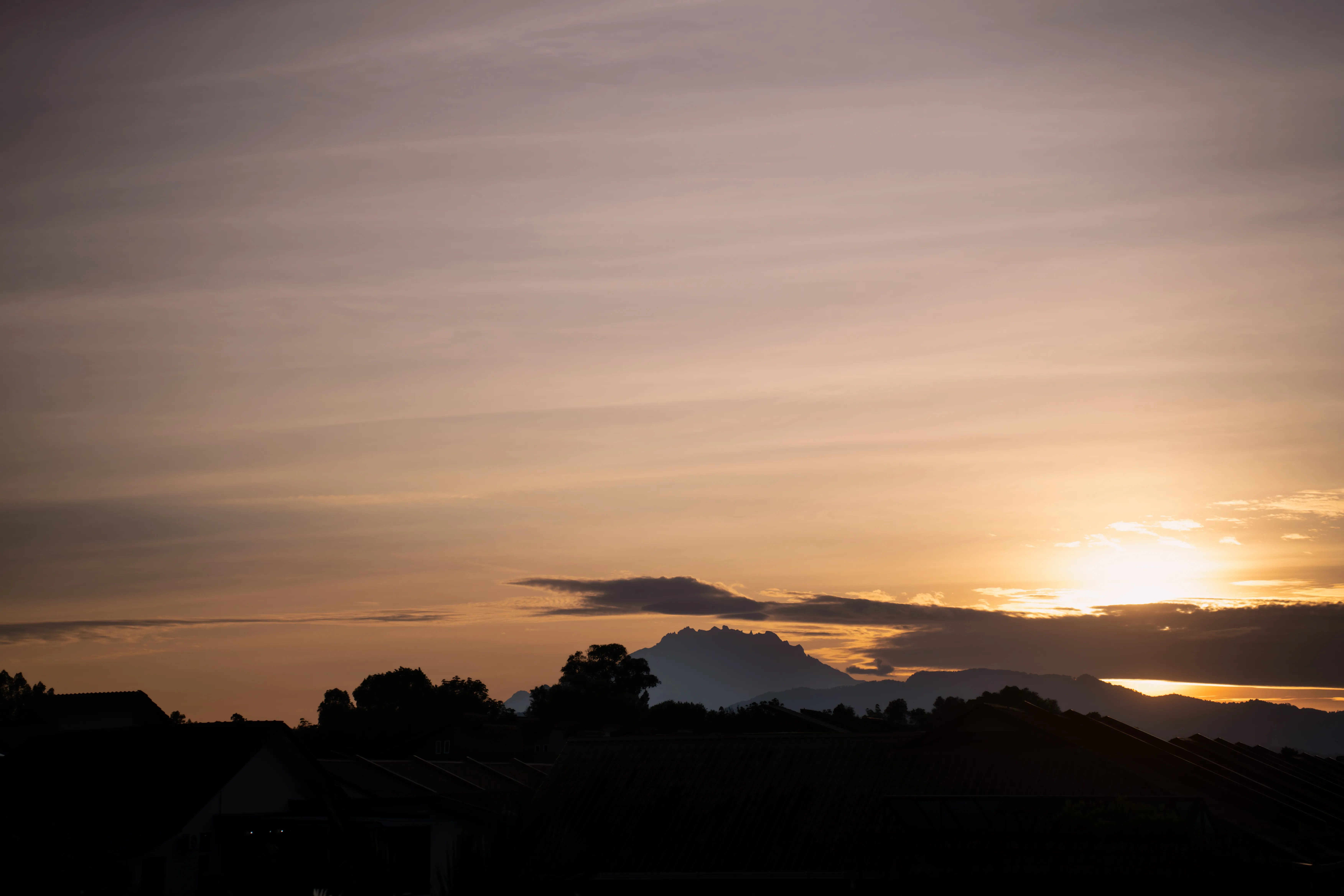 Mount Kinabalu silhouetted beneath a warm sunset sky above dark rooftops